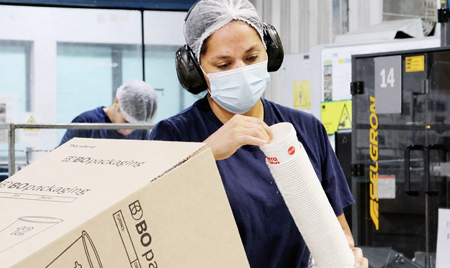 Operaria de BOPackaging manipulando vasos de papel junto a una caja de la marca en la planta de Foodservice
